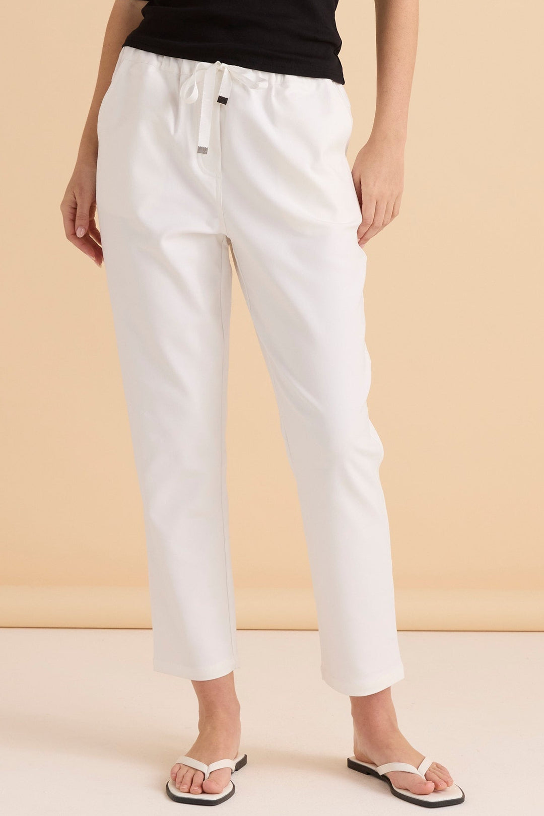 Person wearing white betty basics kenzie pants and a black top on a beige background