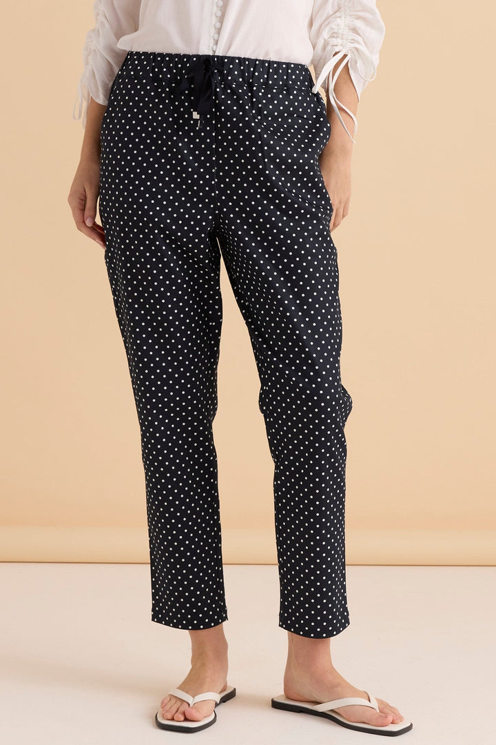 Person wearing navy betty basics kenzie pants with white polka dots on a beige background