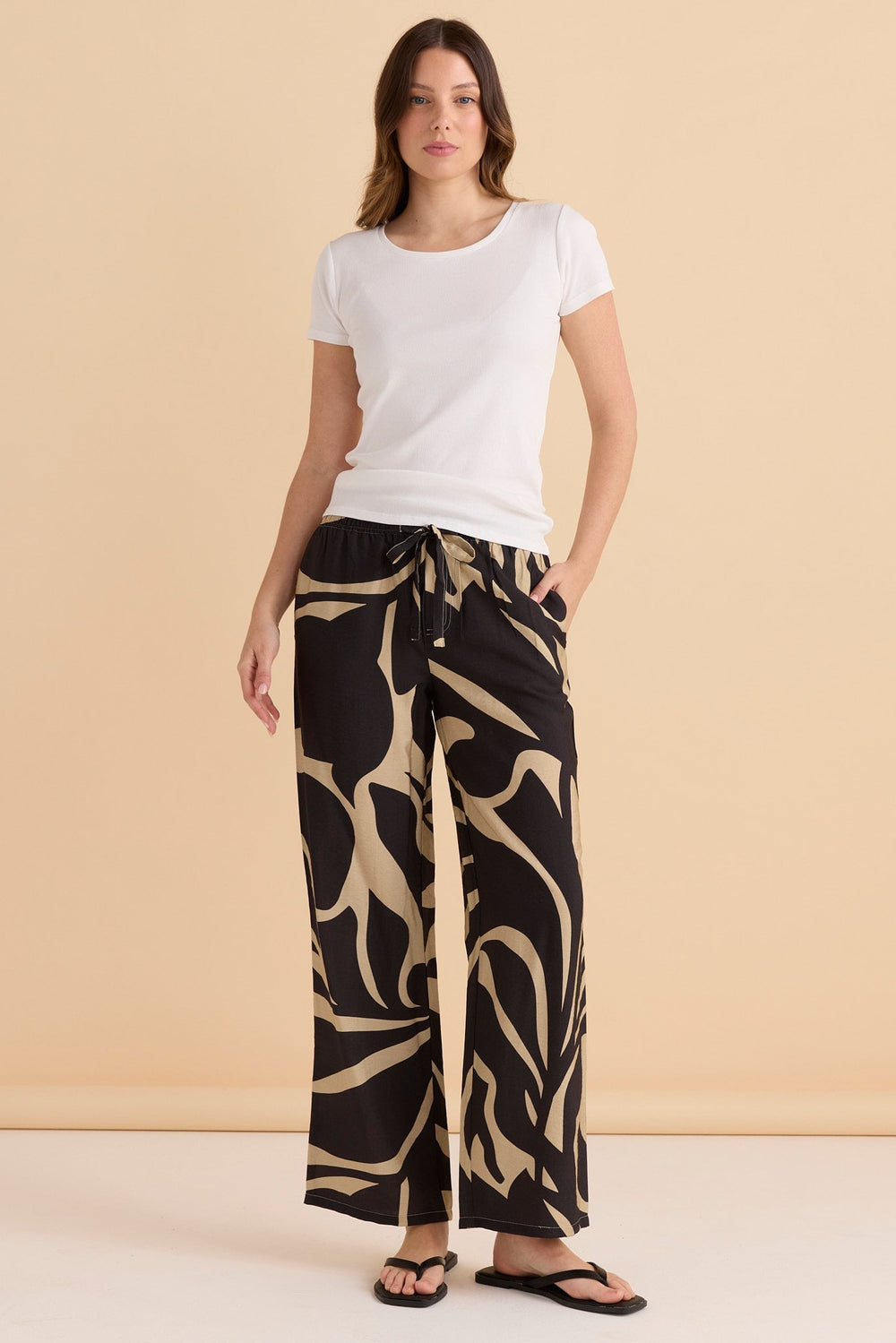 Woman wearing a white t-shirt and patterned black and beige betty basics sutton pants against a beige background