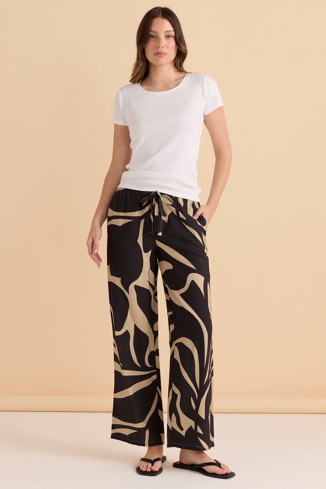 Woman wearing a white t-shirt and patterned black and beige betty basics sutton pants against a beige background