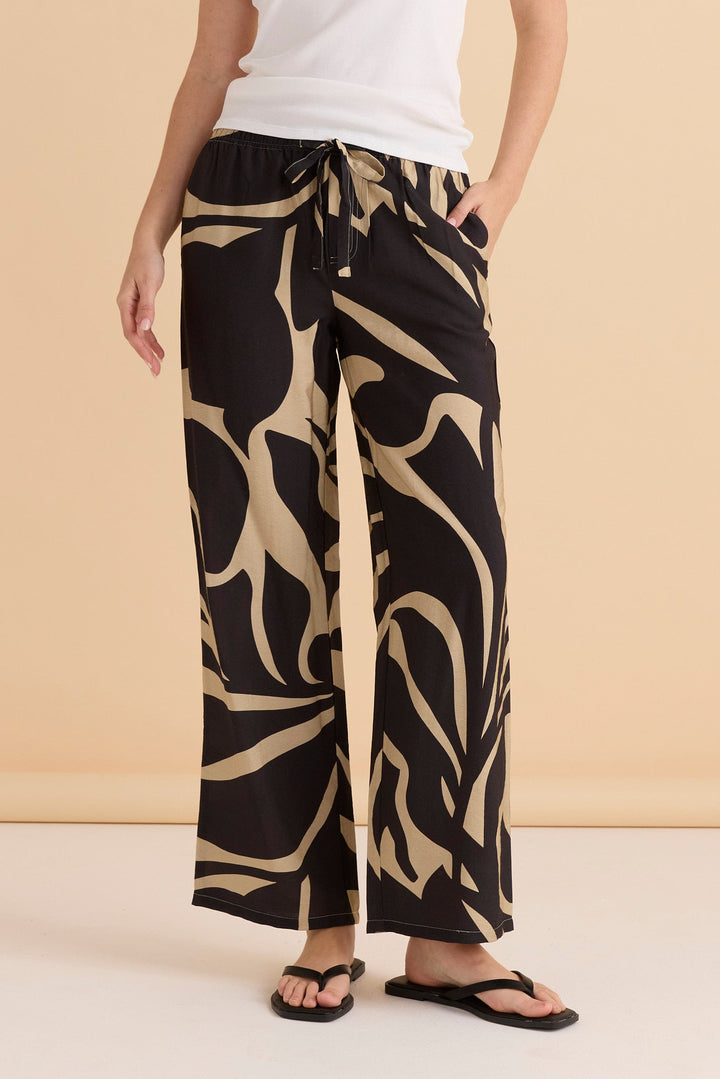 Lady wearing black and beige patterned Betty Basics Sutton pants on a beige background