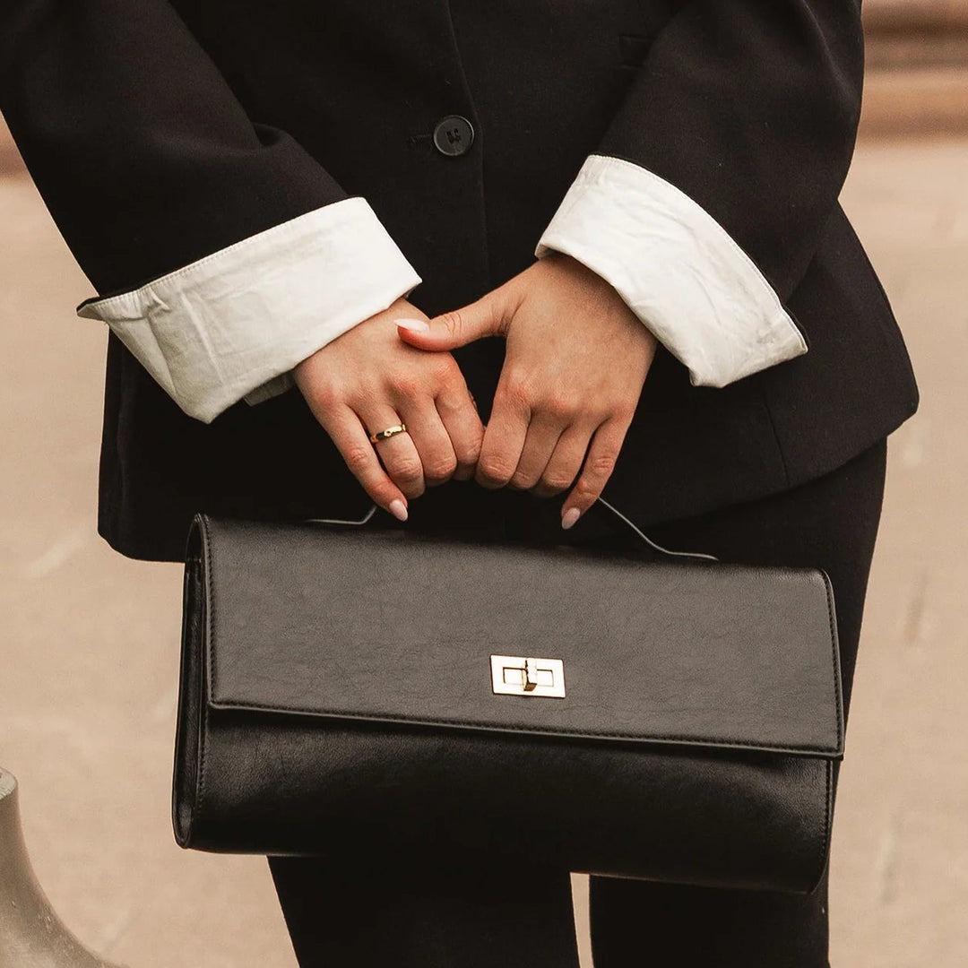 Person holding a black clutch bag with a blurred background