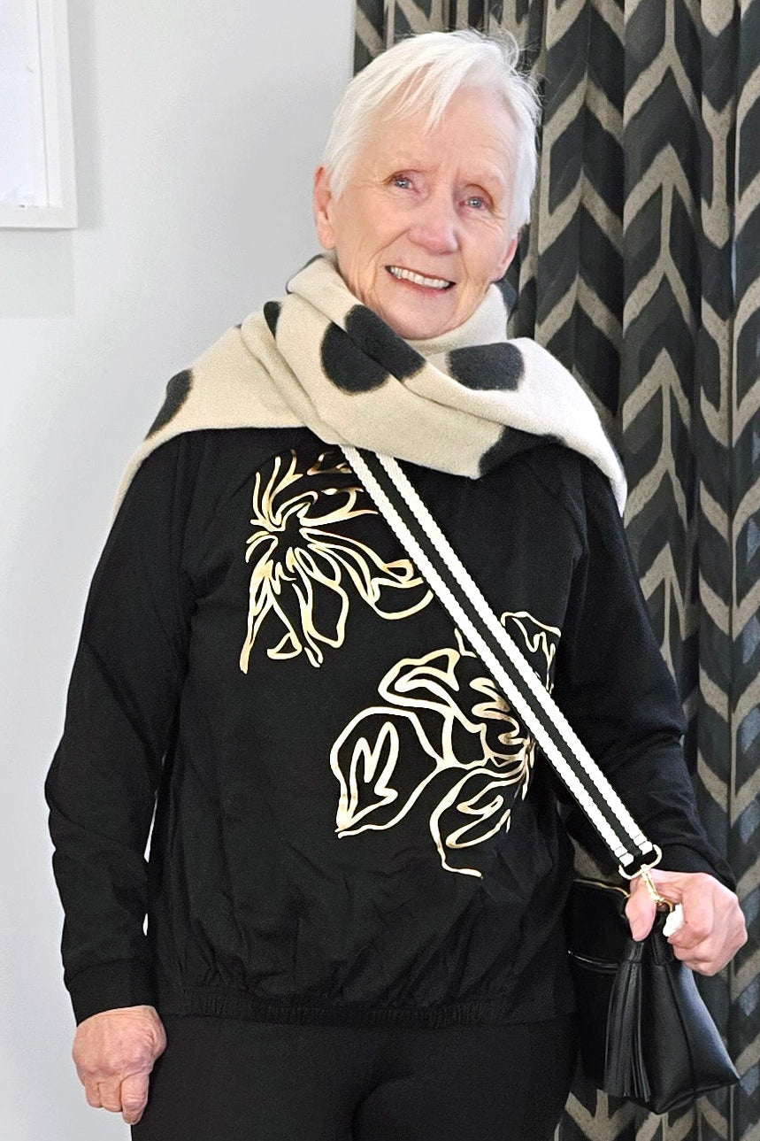 Person wearing a black outfit with floral patterns, holding a walking stick indoors.