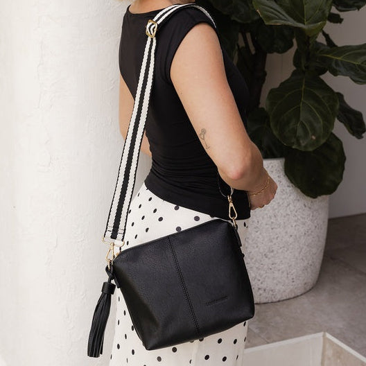 Woman holding a black crossbody bag in a minimal indoor setting