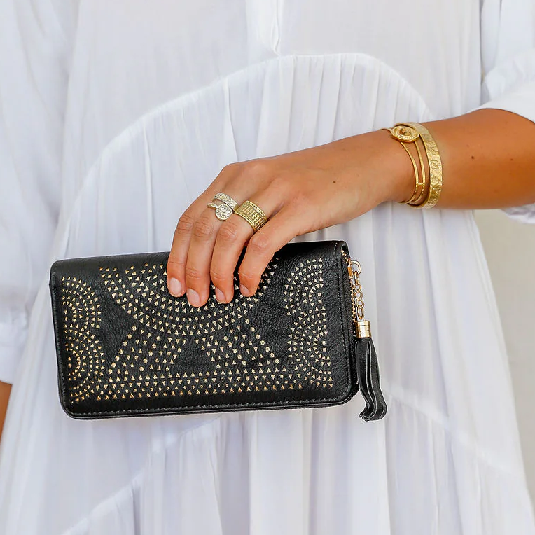 Person wearing a white outfit holding a black clutch with gold accents.