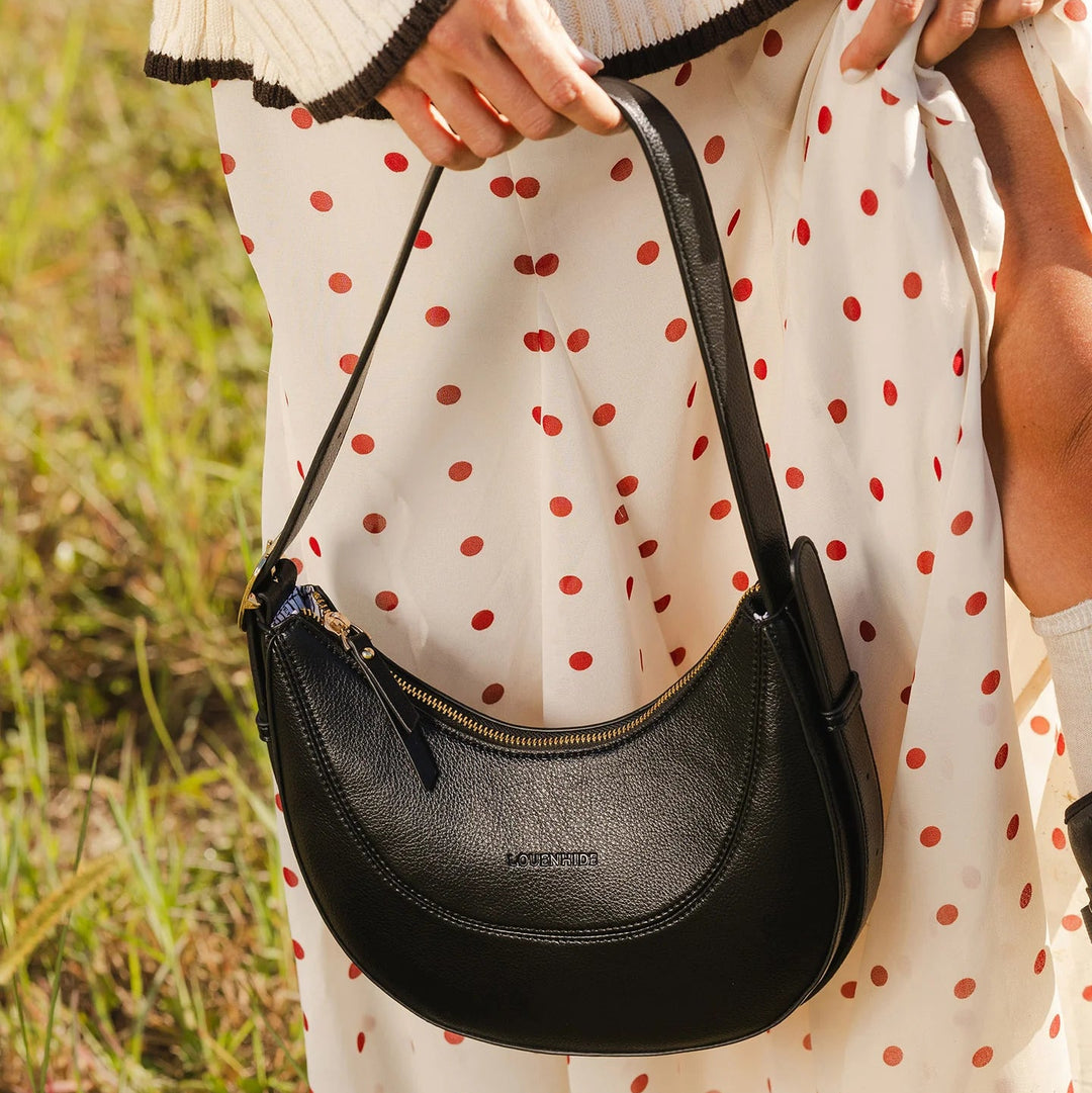 Person holding a black handbag with a polka dot dress in the background