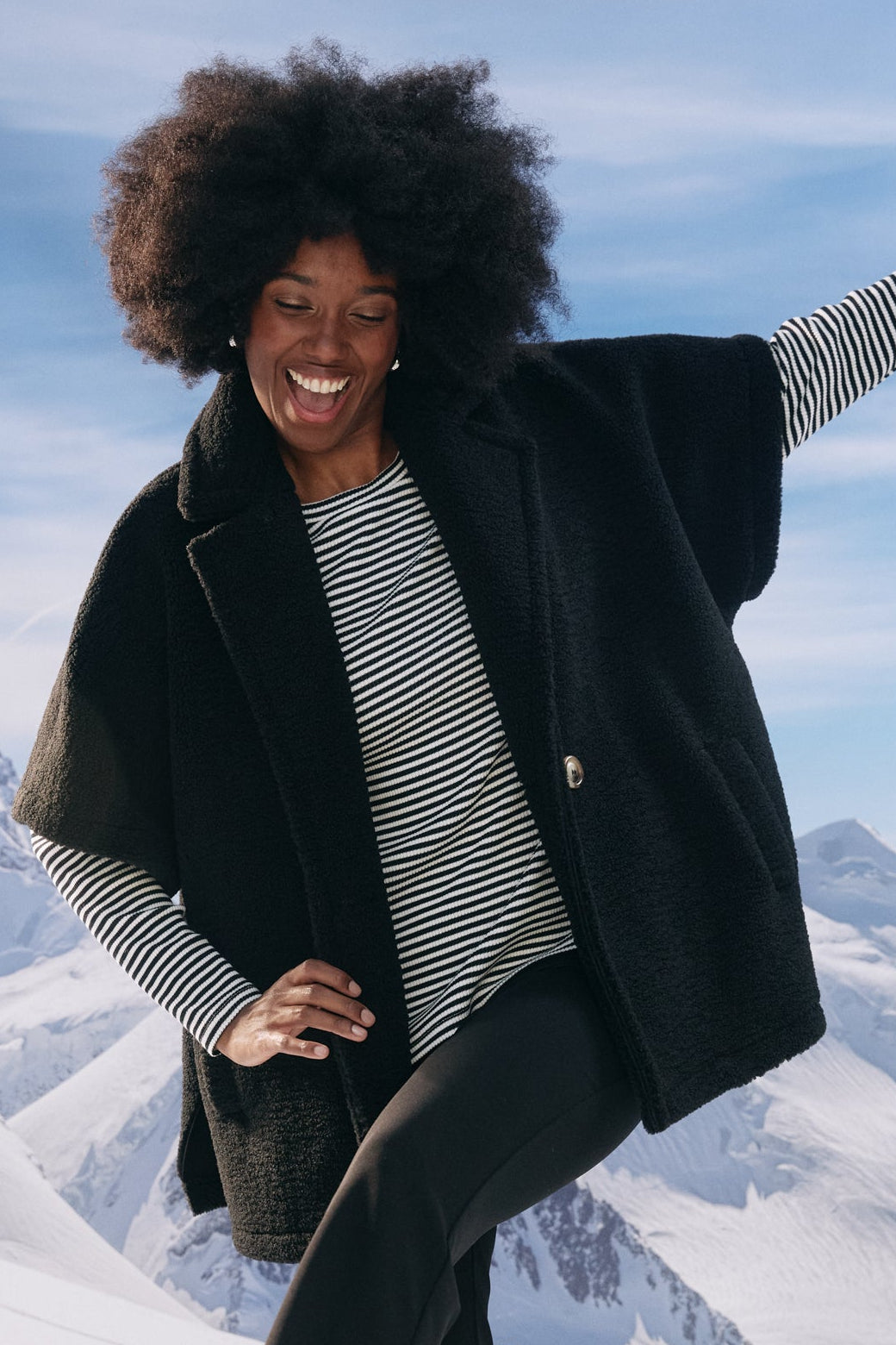Person in winter clothing posing in front of snowy mountains