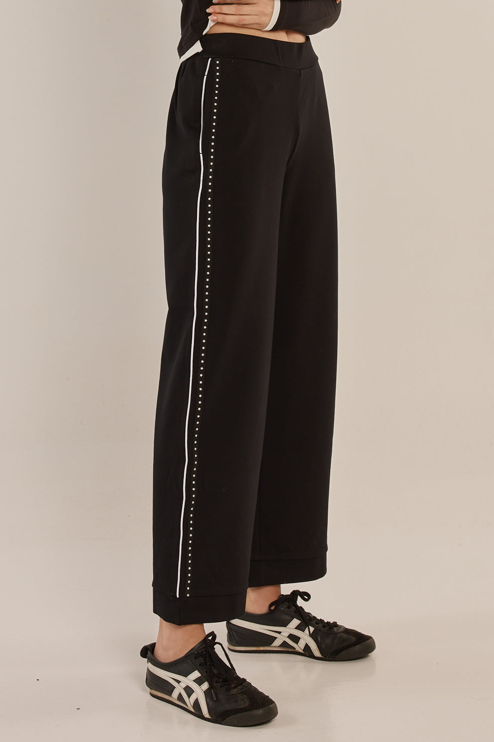 Black pants with white trim worn by a person on a beige background