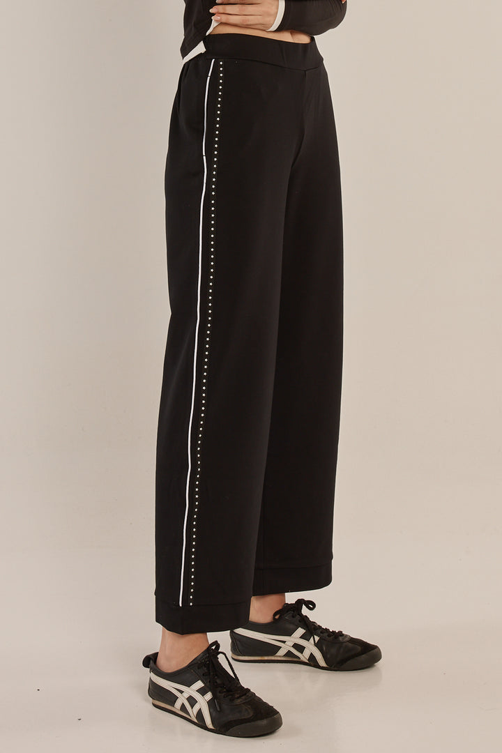 Black pants with white trim worn by a person on a beige background