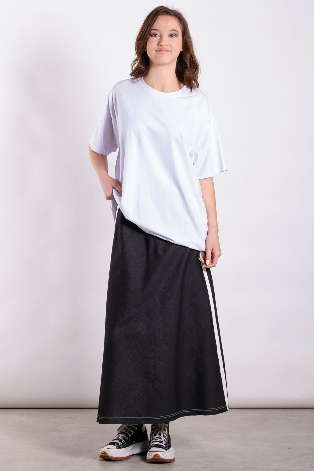 Person wearing a white oversized t-shirt and black skirt with white stripes on a plain background