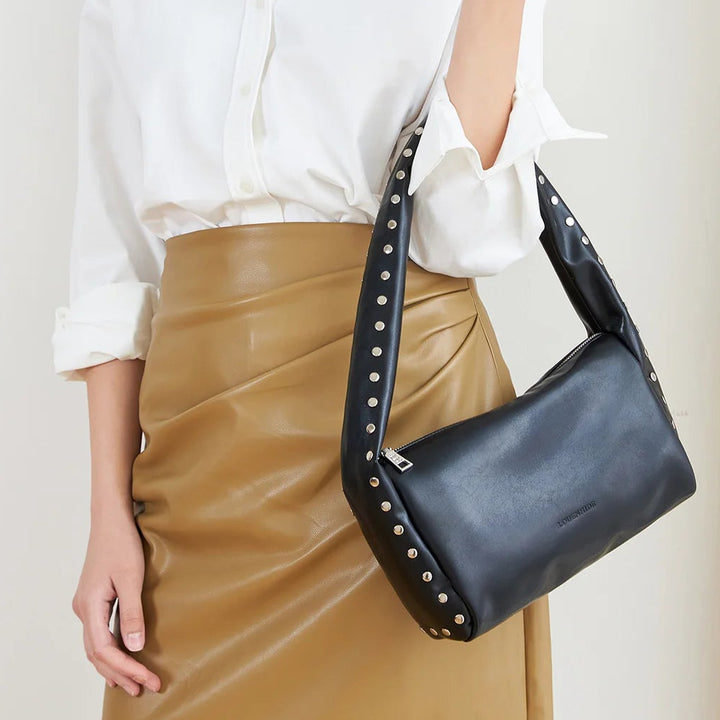 Woman holding a black handbag against a plain background