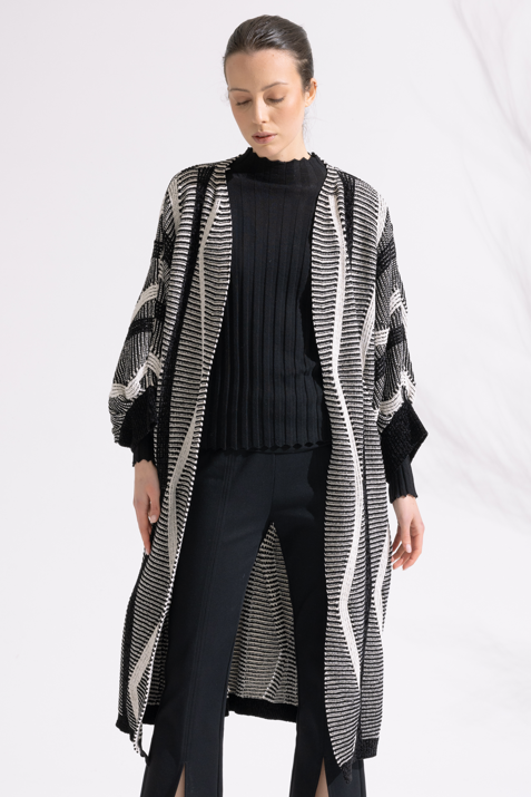 Person wearing a black and white patterned cardigan over a black outfit on a white background