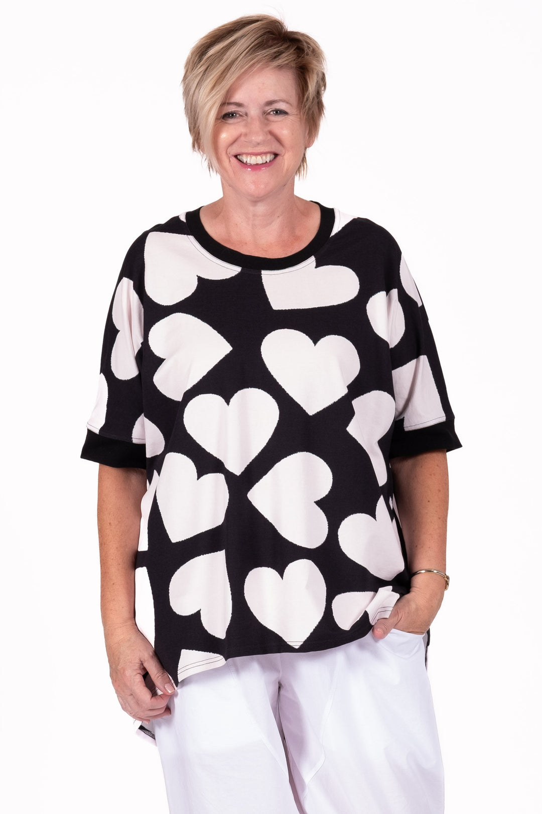 lady wearing black & white heart relaxed tee with whita pants on a white background