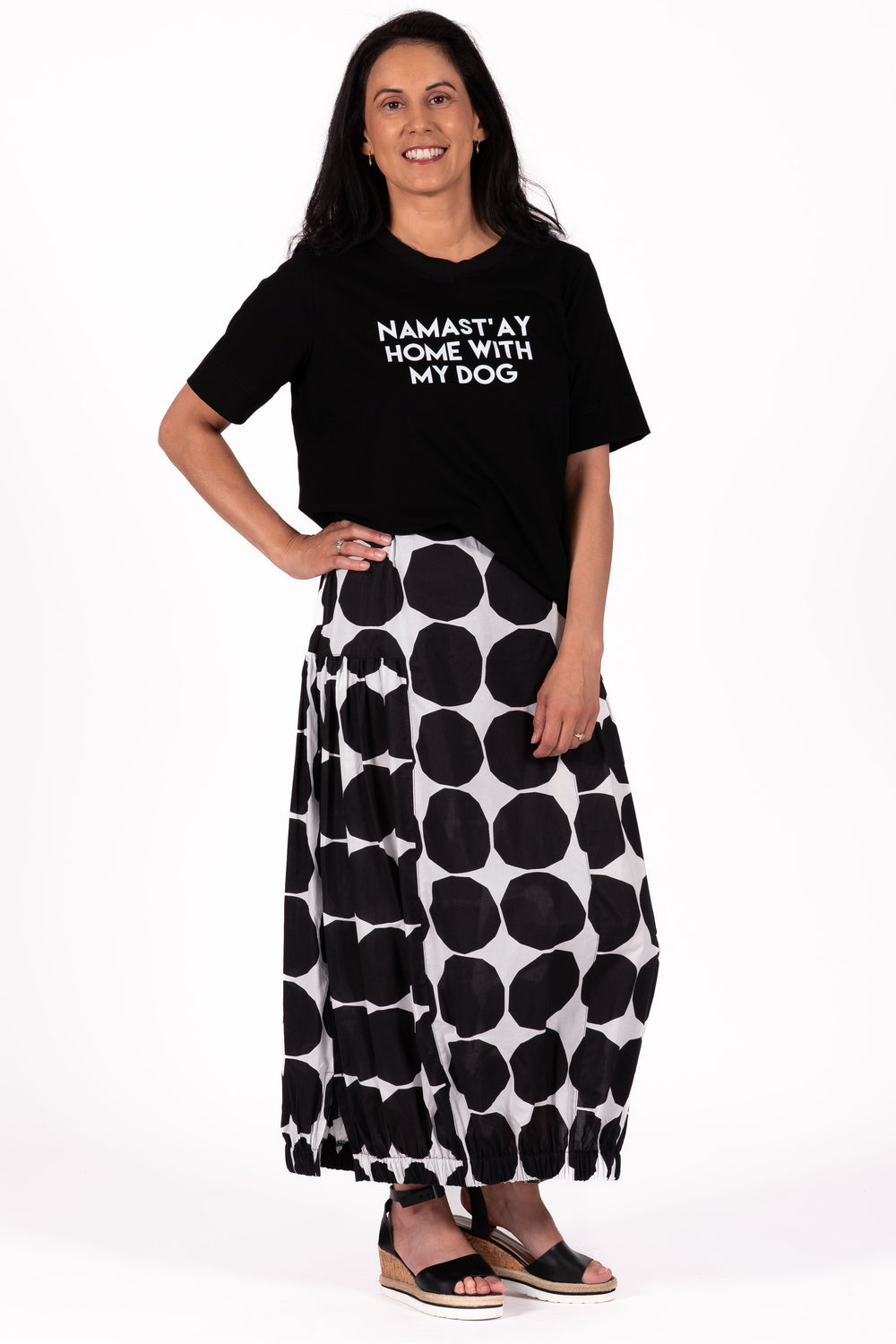 Woman wearing a black t-shirt with text and a black and white polka dot skirt on a white background