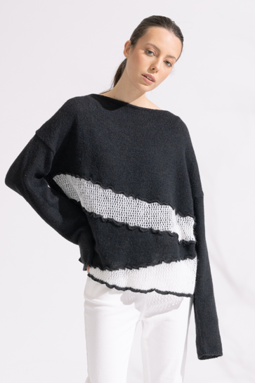 Person wearing a black and white sweater with white pants on a white background