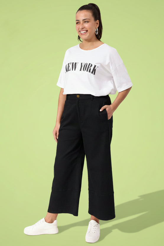 Woman wearing a white 'New York' t-shirt and black wide-leg pants on a white background