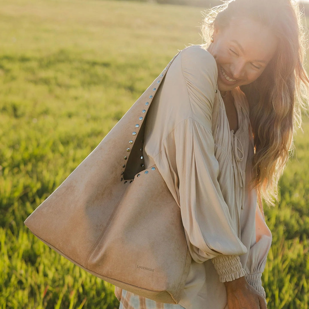 Woman holding a beige tote bag in a grassy field