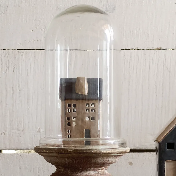 Small model house inside a glass dome on a wooden base against a textured white wall.