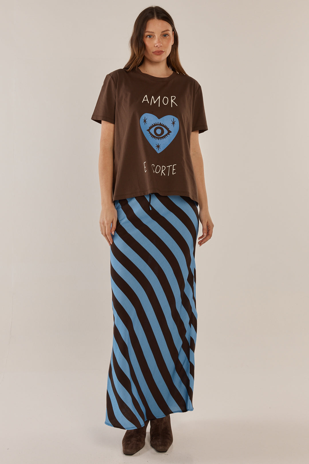 Woman wearing a brown t-shirt with a graphic design and a long black and blue striped skirt on a beige background