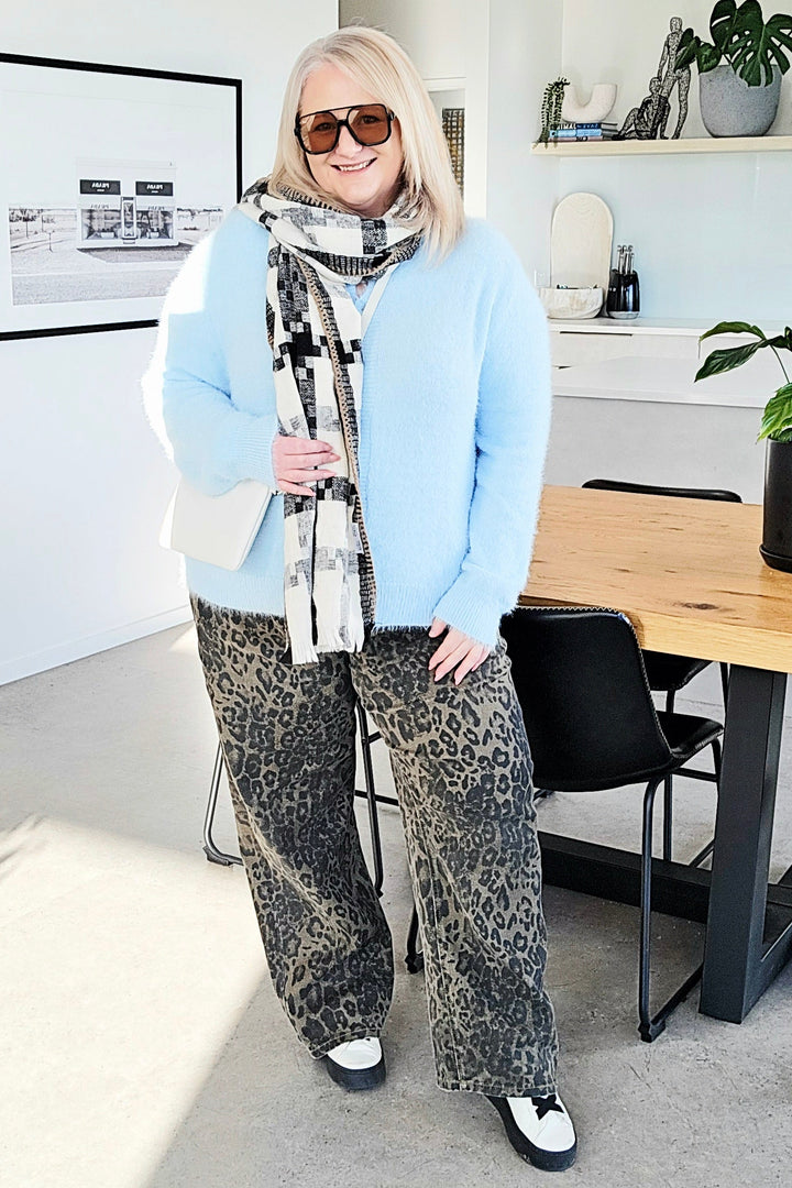 Woman standing in a modern office space wearing sunglasses and a light blue sweater.