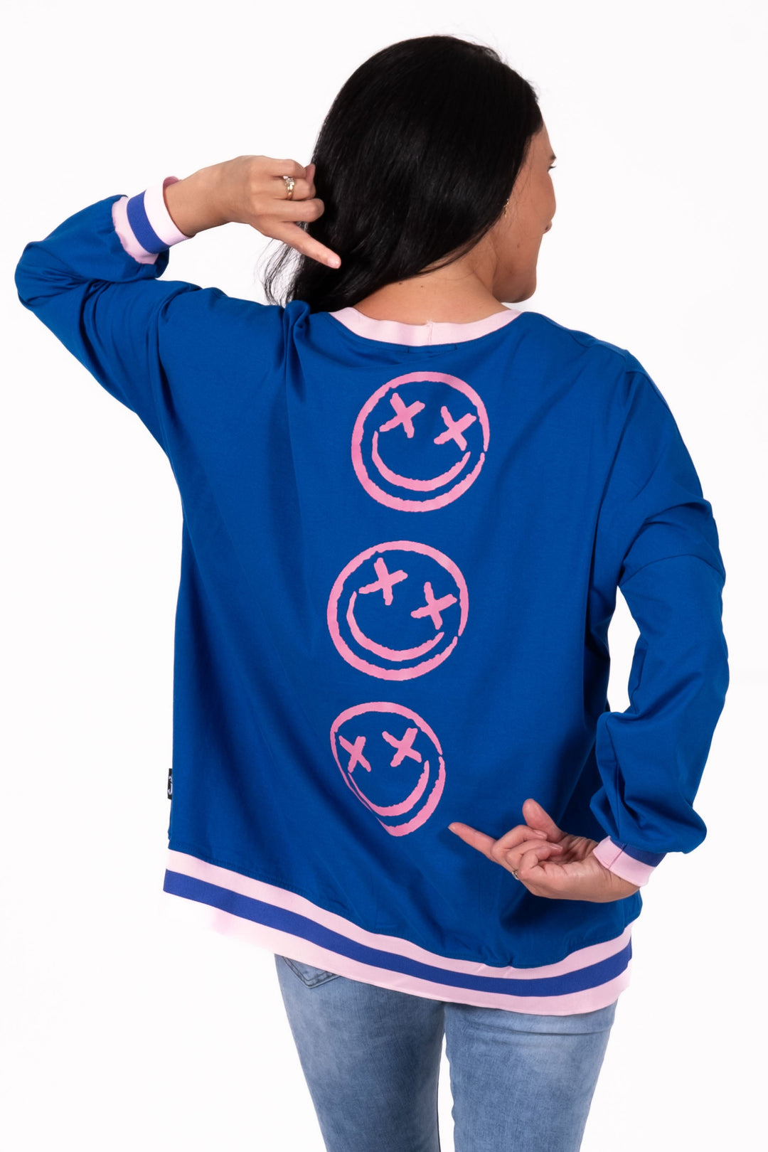 Person wearing a blue sweatshirt with pink smiley face designs on the back, standing against a white background.