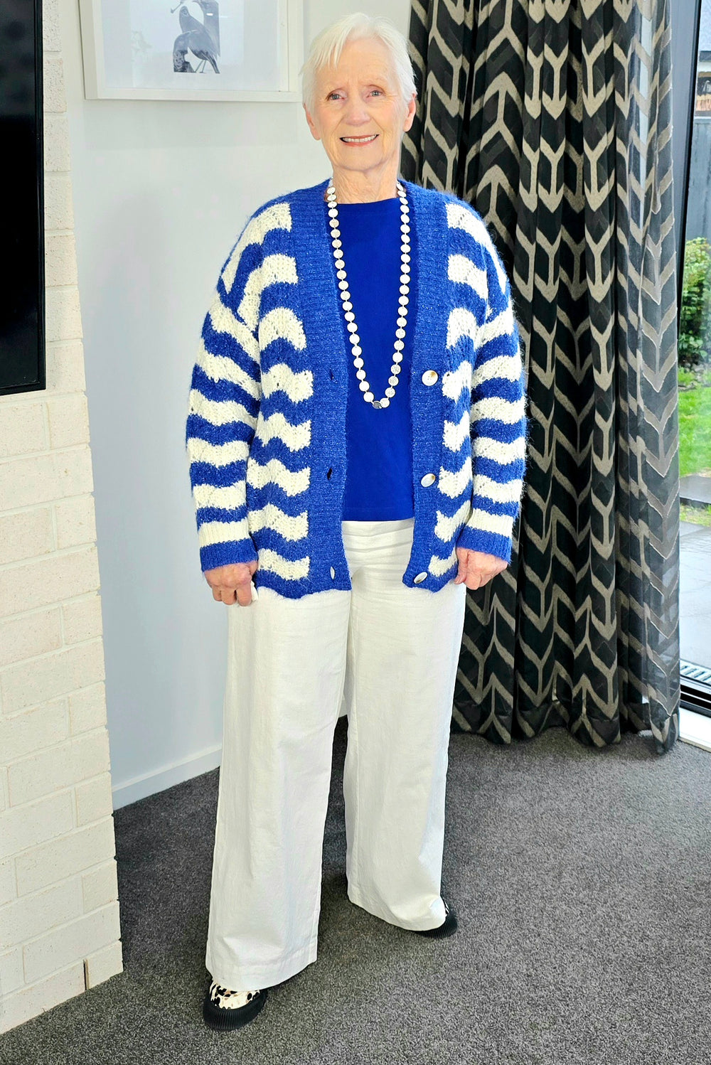 Woman wearing a blue and white striped cardigan, blue shirt, and white pants indoors.