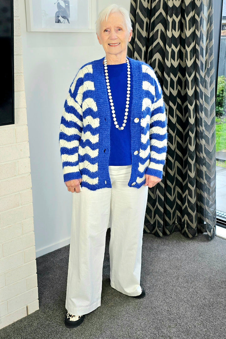 Woman wearing a blue and white striped cardigan, blue shirt, and white pants indoors.