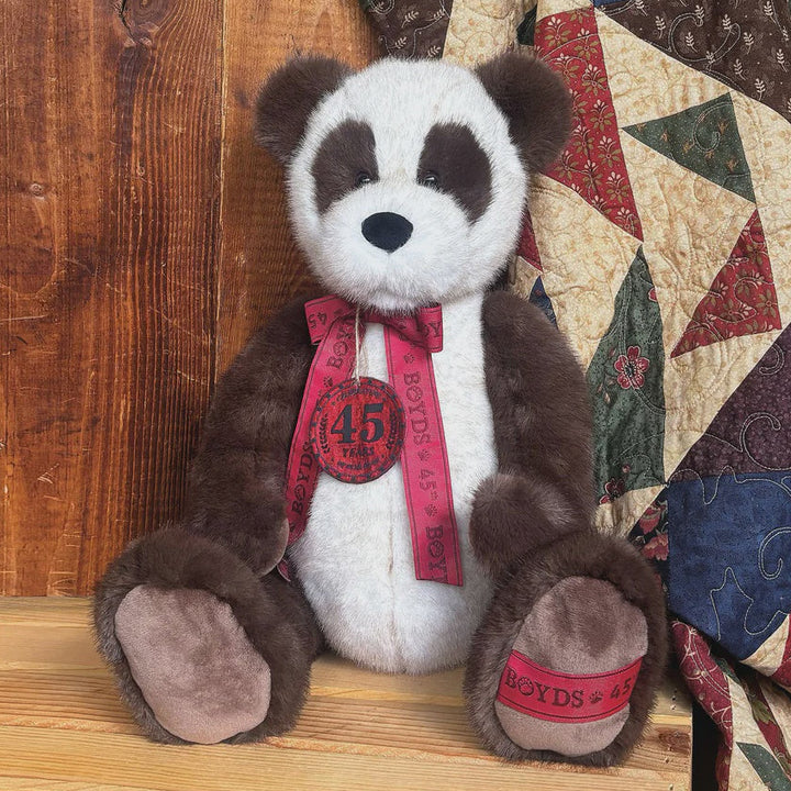 Stuffed panda bear with a red ribbon sitting on a wooden surface next to a quilt.