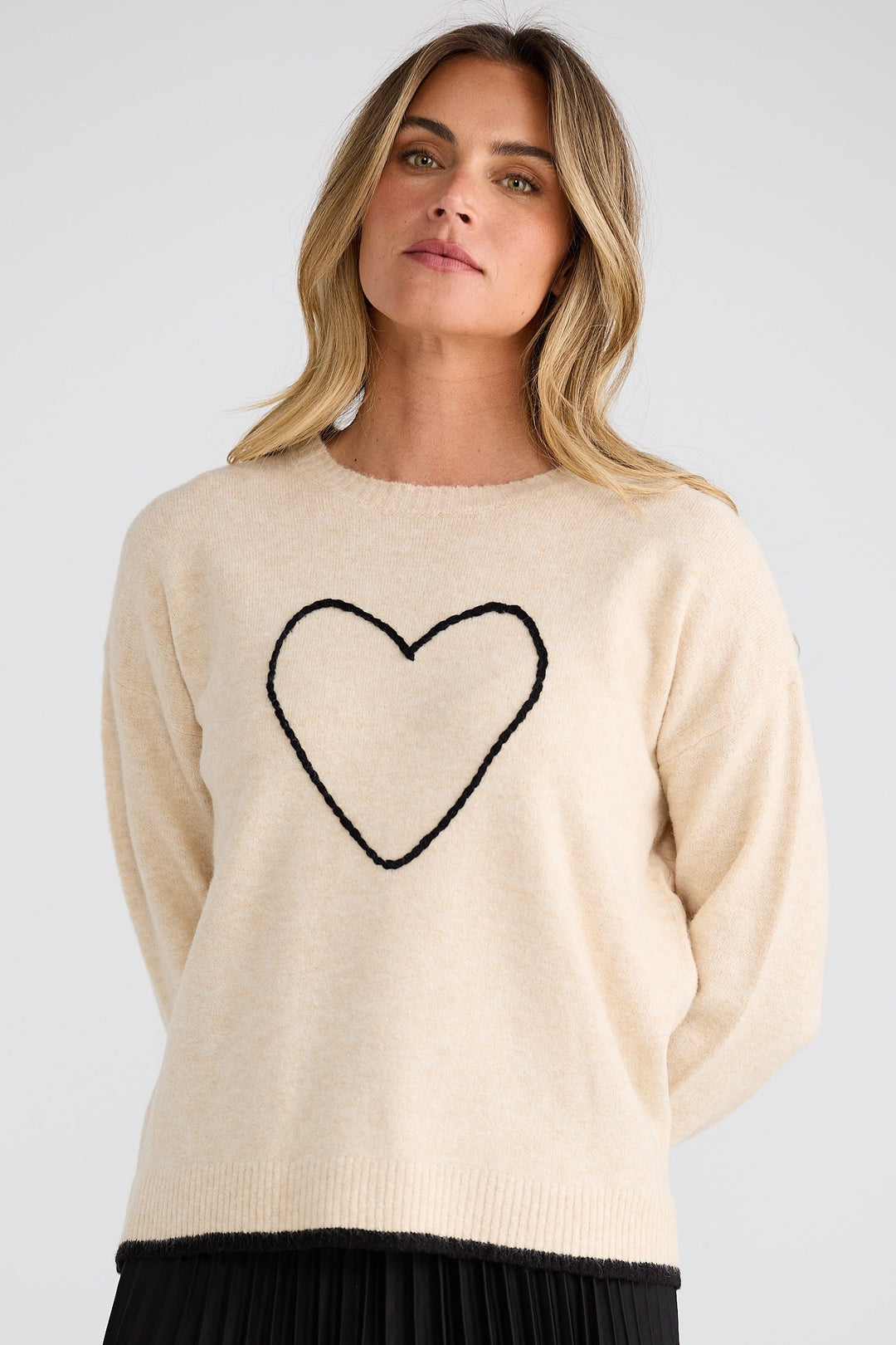 Woman wearing a beige sweater with a black heart design on a plain background