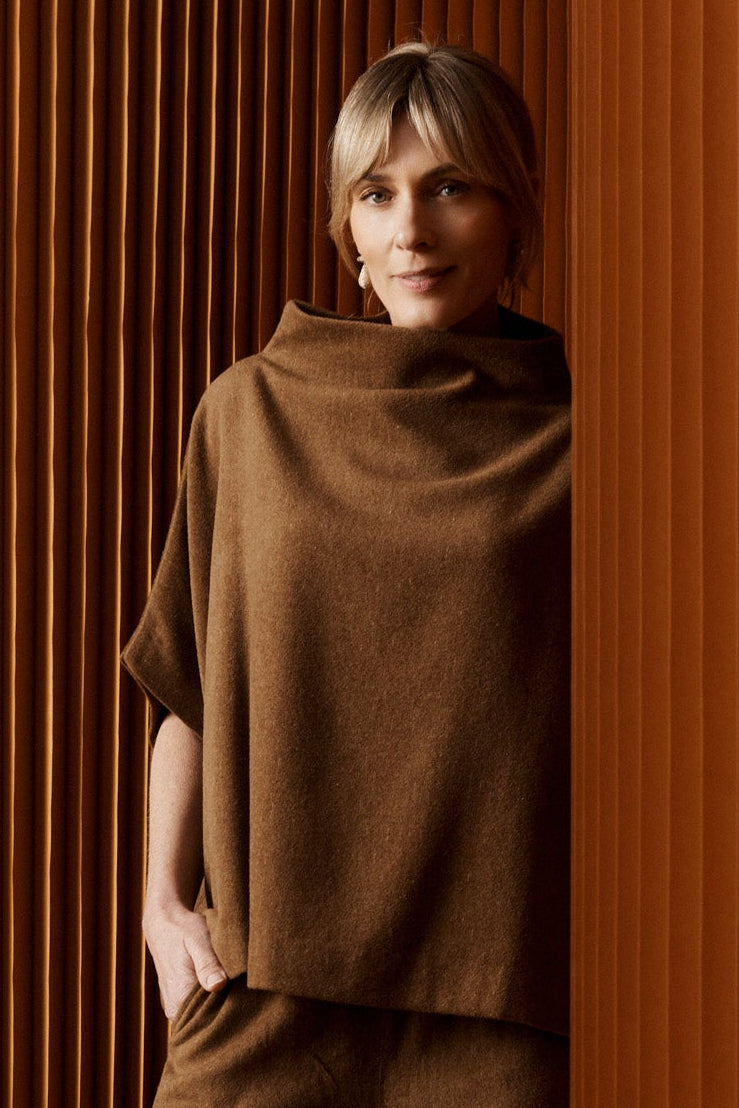 Woman in a brown outfit standing against a textured wall.