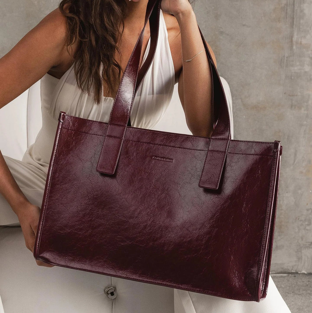 Woman holding a large burgundy leather tote bag against a neutral background
