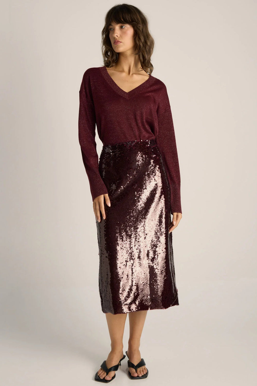 Woman wearing a burgundy sweater and sequin skirt on a plain background