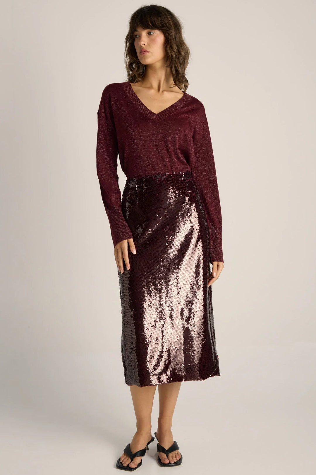 Woman wearing a burgundy sweater and sequin skirt on a plain background