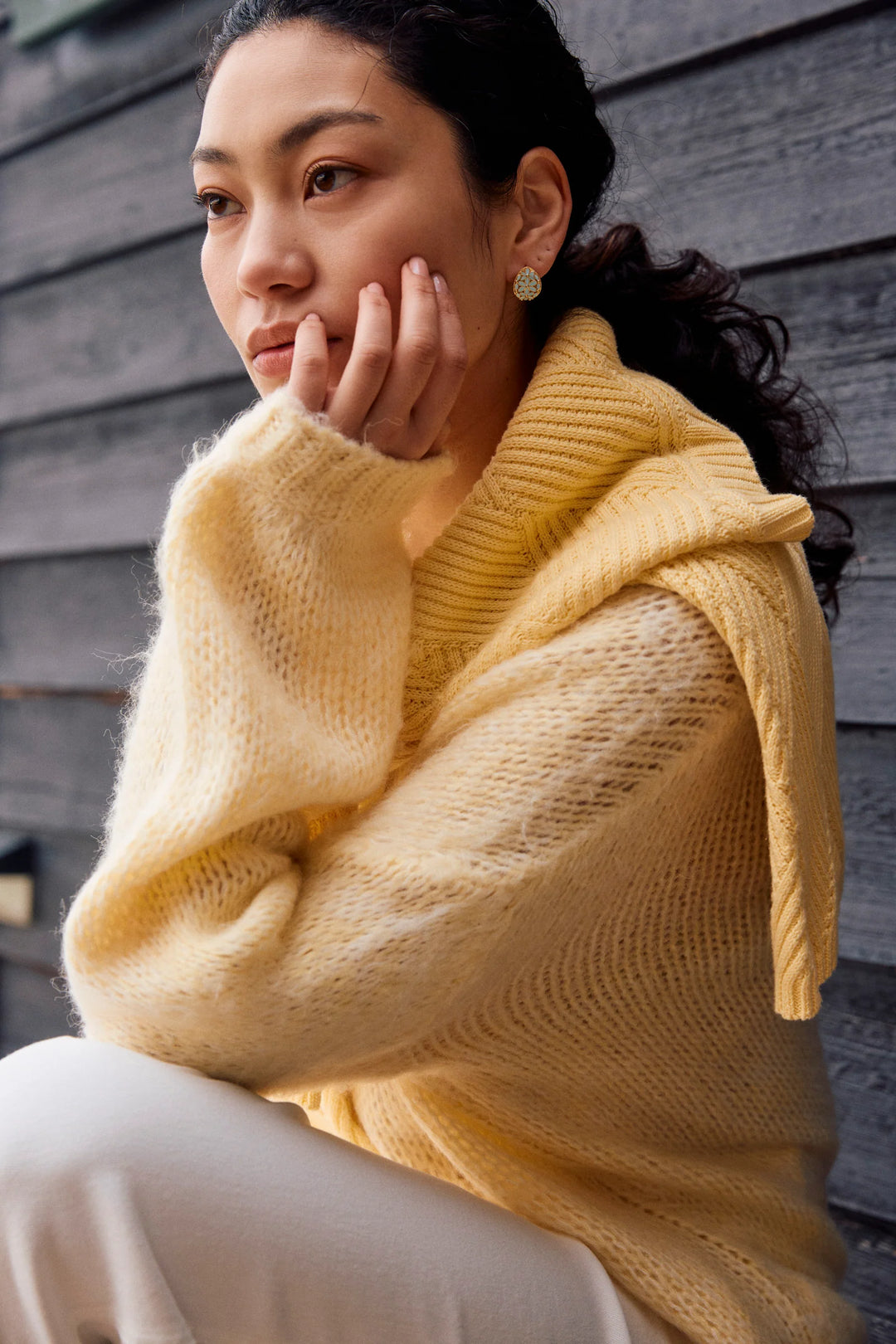 Woman wearing a yellow sweater sitting against a wooden wall.