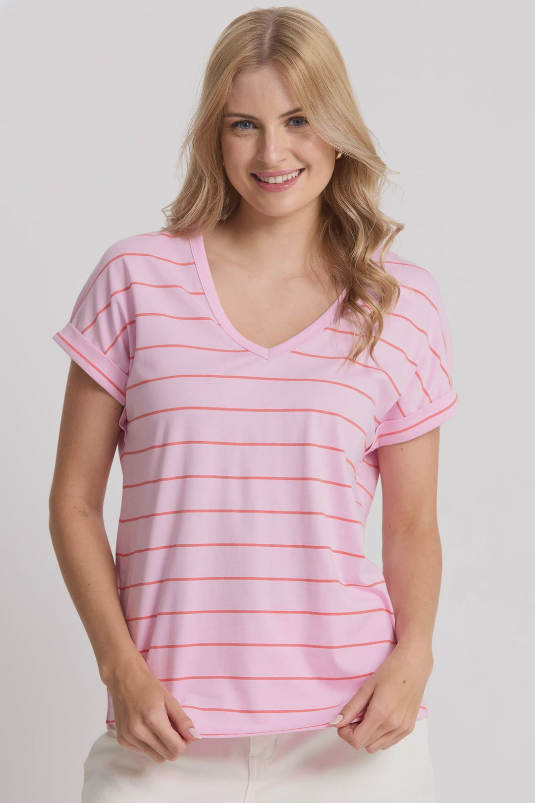 Woman wearing a pink striped shirt and white pants on a plain background
