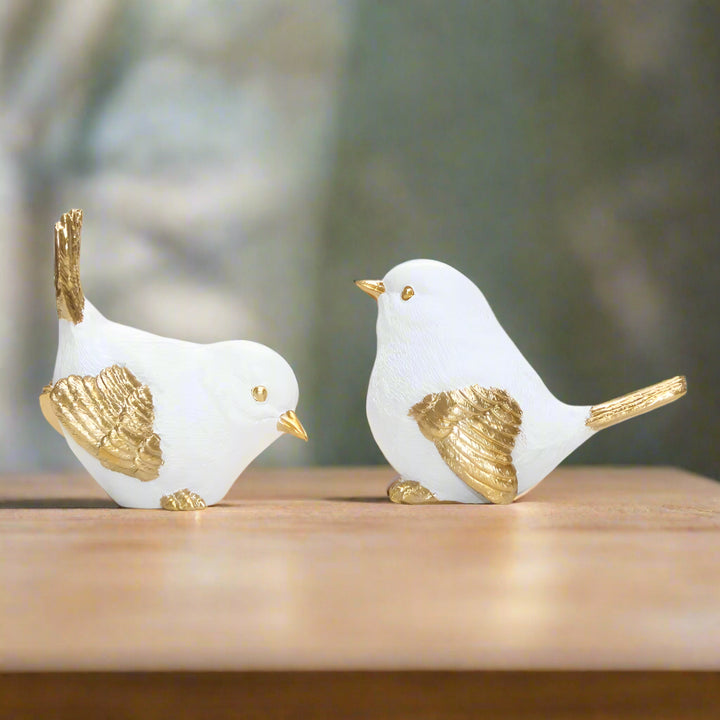 Two white ceramic birds with gold accents on a white background