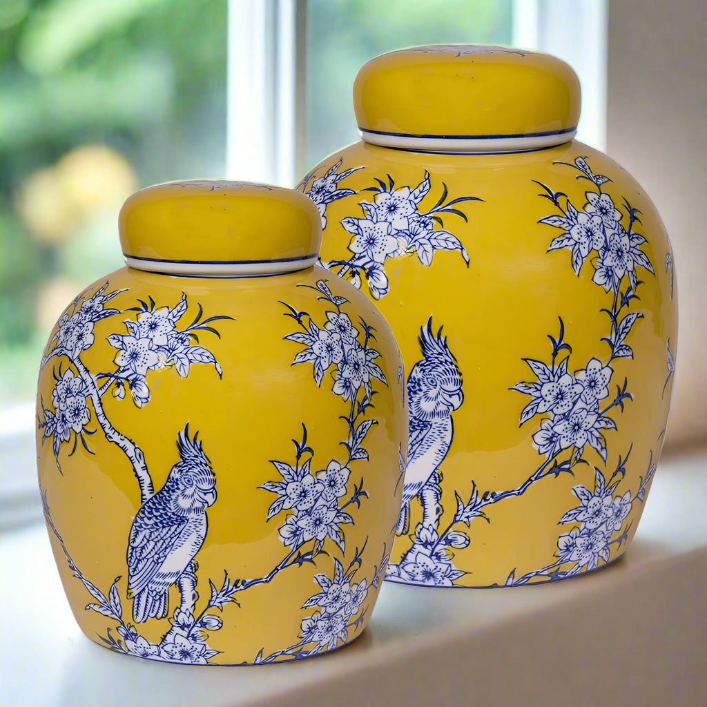 Two yellow ceramic jars with blue floral and parrot patterns on a white background