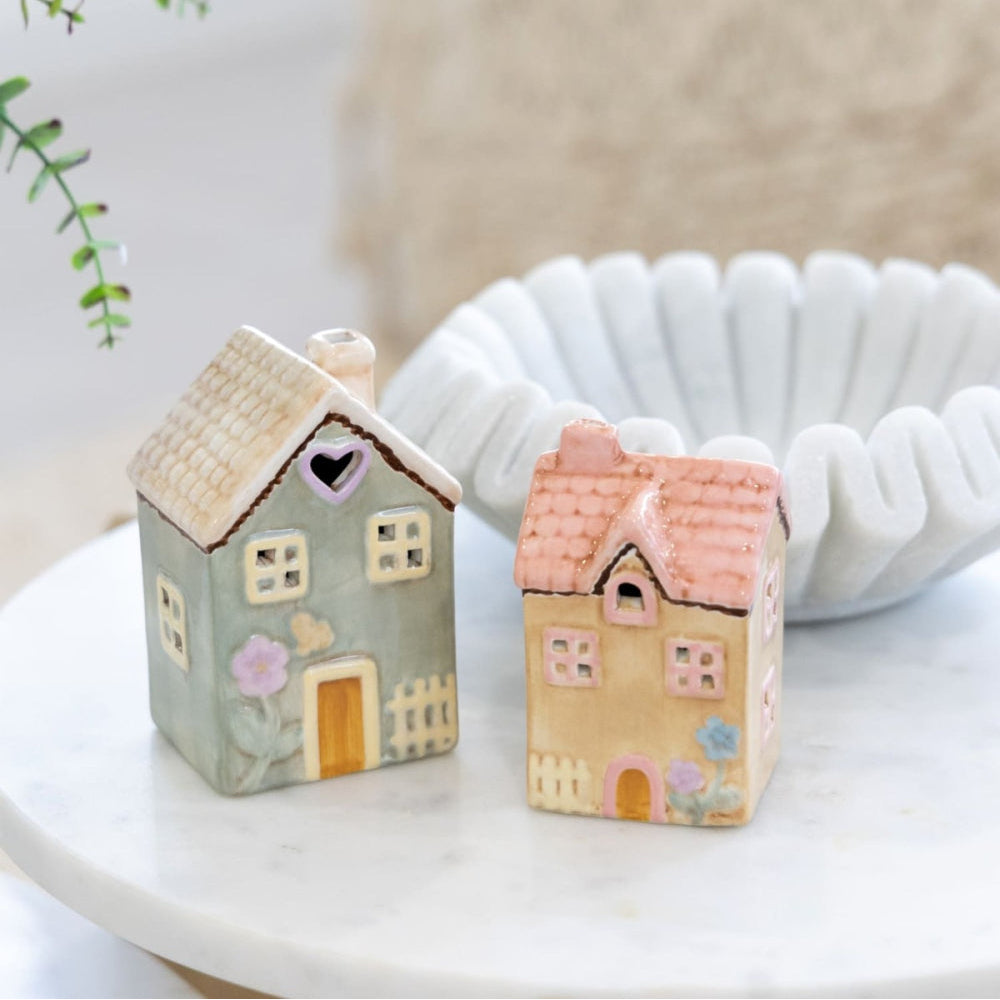Two small house-shaped decorative items on a white surface with a blurred background
