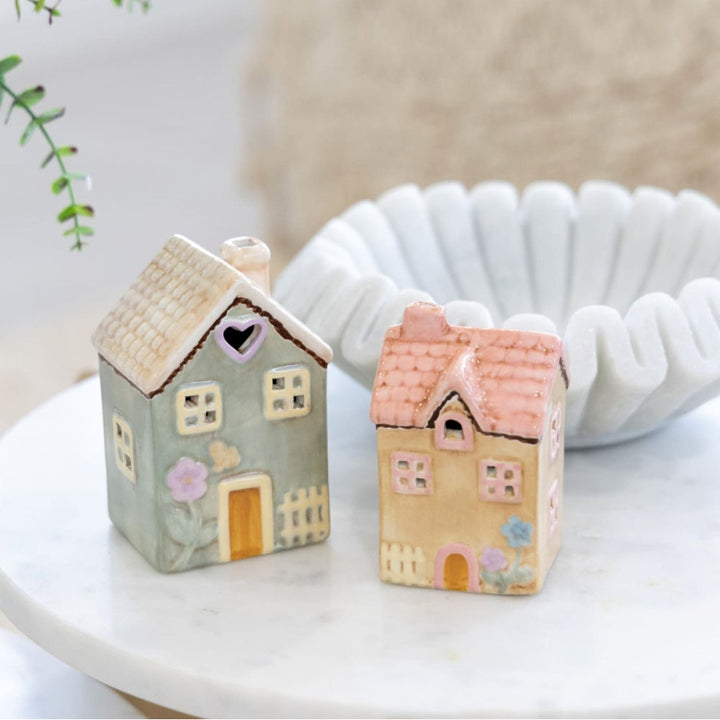 Two small house-shaped decorative items on a white surface with a blurred background