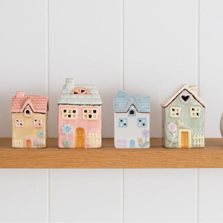 Set of four colorful house-shaped decorative boxes on a wooden shelf against a white paneled wall.