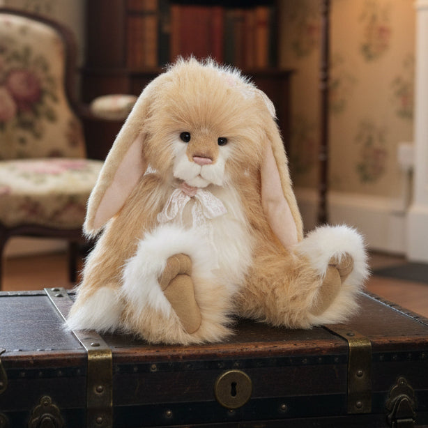 A plush toy resembling a bunny with a warm honey-colored coat, white belly, and long ears, sitting on a green mossy surface.
