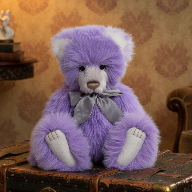A plush purple teddy bear with a gray bow accessory, part of the Charlie Bears collection.