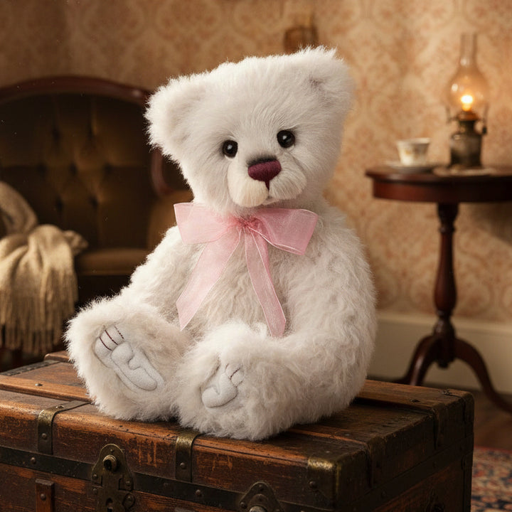 A plush white teddy bear with a pink bow accessory designed by Isabelle Lee, part of the Charlie Bears collection.