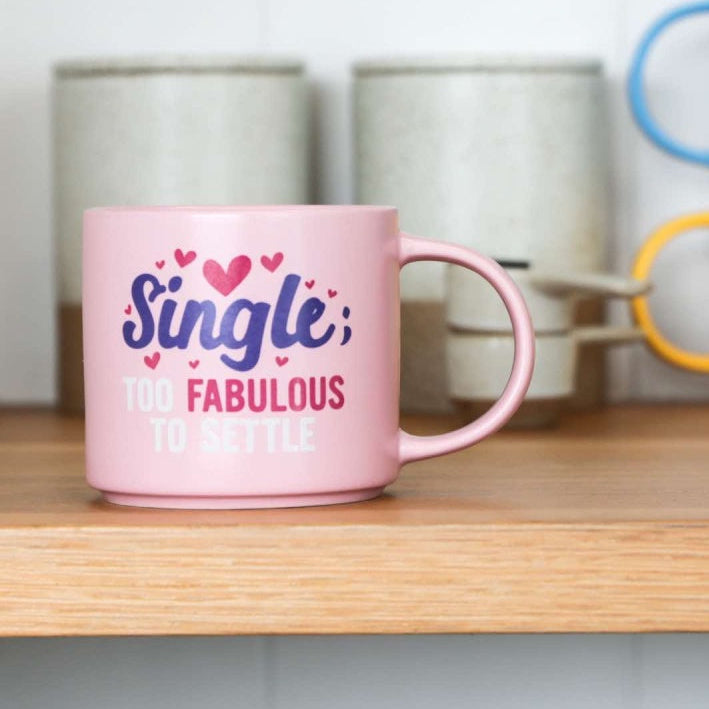Pink mug with 'Single & Fabulous' text on a shelf with other colorful mugs.