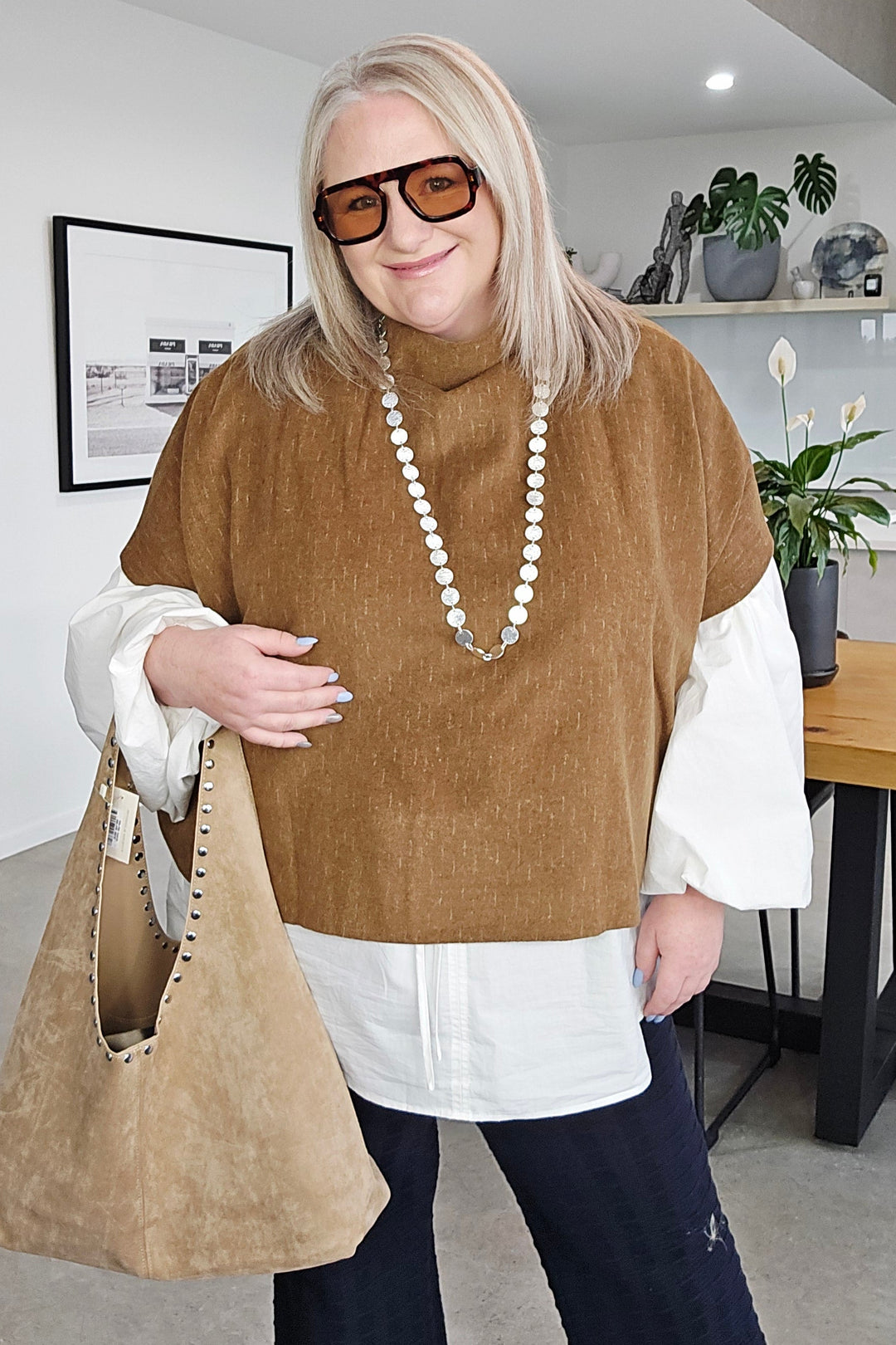 Woman sitting on a chair in an office setting with a desk and computer in the background.