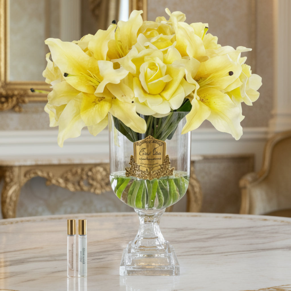 Clear glass vase with yellow flowers and two small bottles on a white background