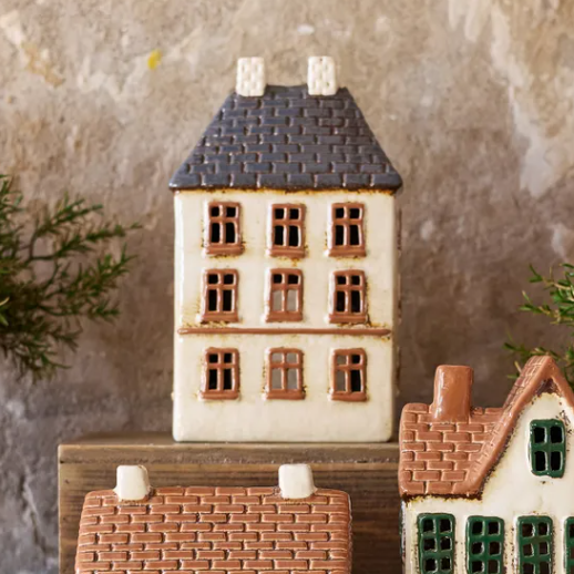Set of ceramic house-shaped boxes on a wooden surface with a stone wall background