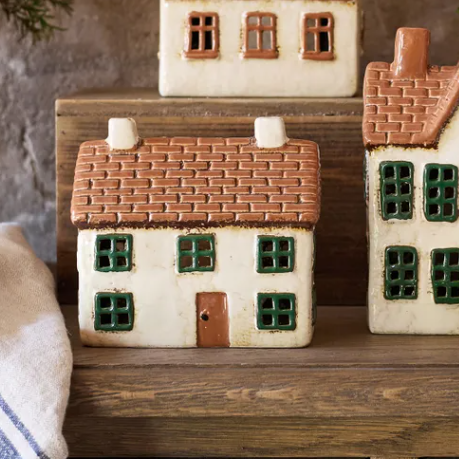 Set of ceramic house-shaped boxes on a wooden surface with a stone wall background