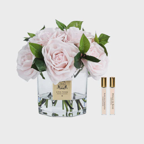 Cote Noire floral arrangement in a glass vase with two perfume bottles on a white background