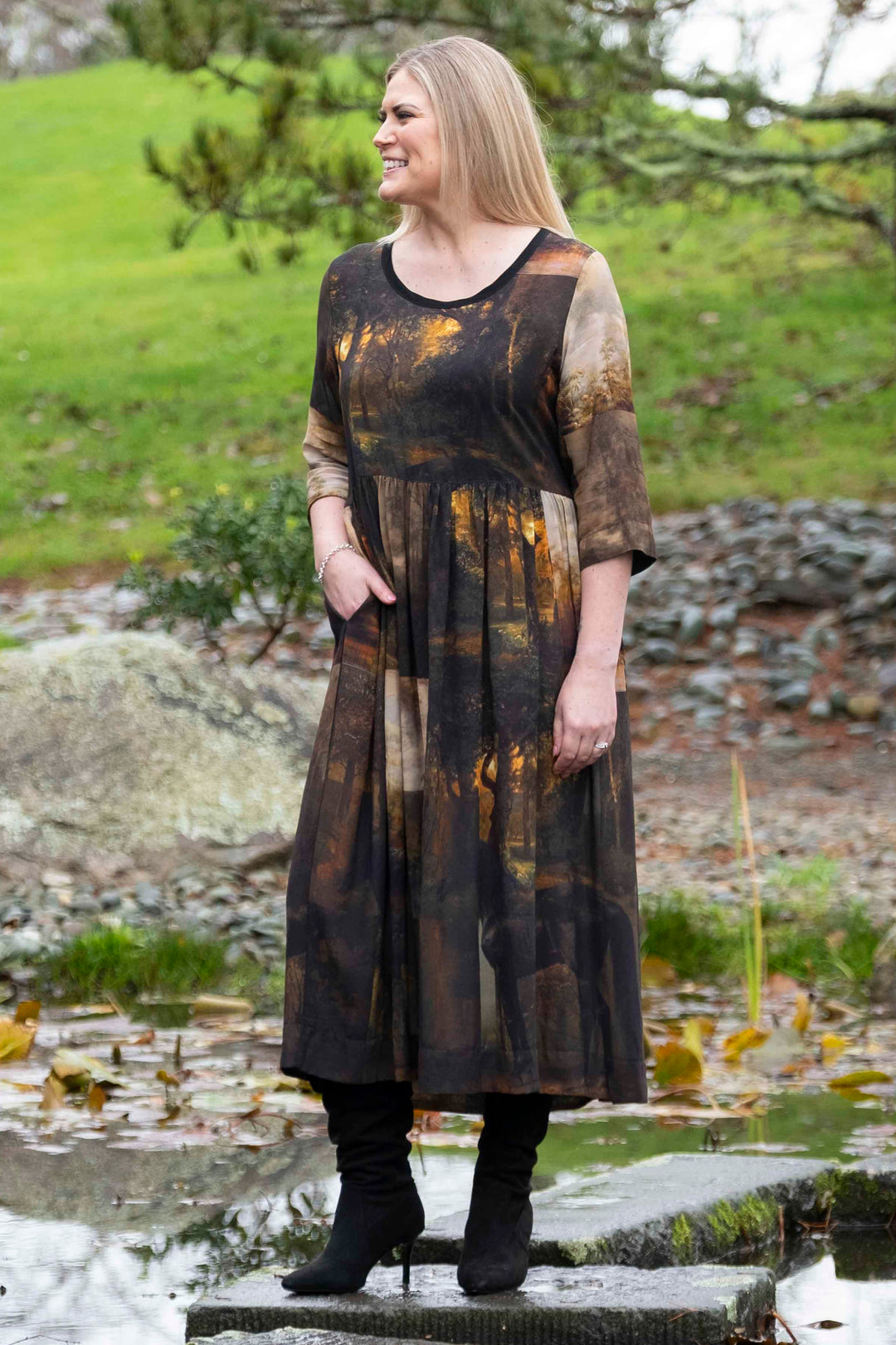 Woman standing by a pond in a long, dark deeanne hobbs tarbana dress with a patterned design created by deeanne hobbs, nz artist.